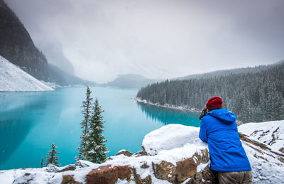 Rear view of man standing by snow on retaining wall against frozen lake