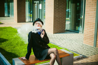 Young woman smoking while sitting on bench at park