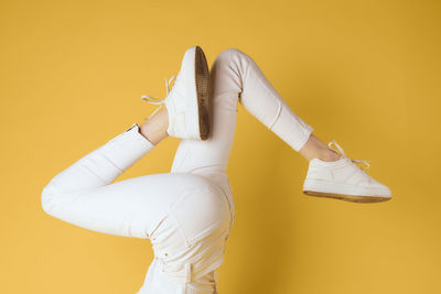 Low section of woman holding hands against yellow background