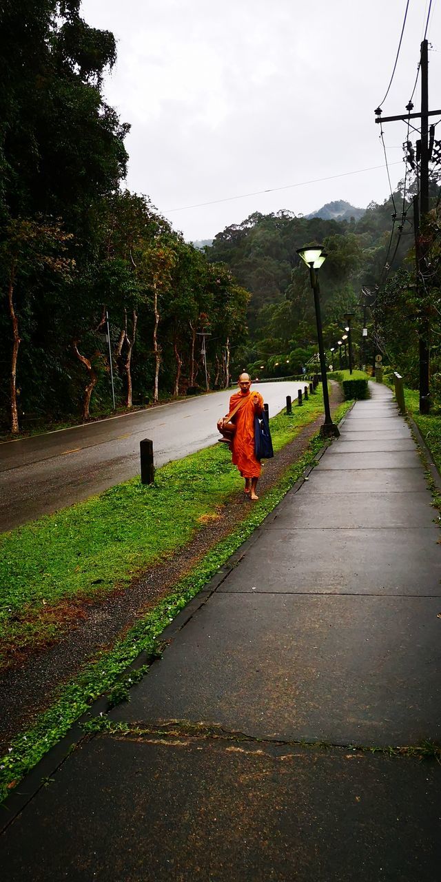 PERSON ON FOOTPATH BY ROAD AGAINST SKY