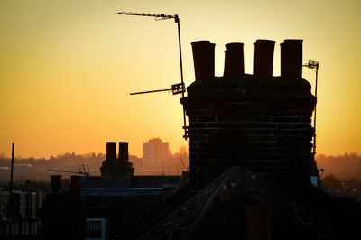 Silhouette of chimneys against sky during sunset