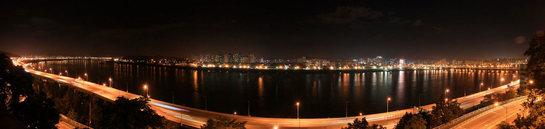 Panoramic view of river against sky in illuminated city at night