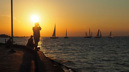 Silhouette people at beach against sky during sunset