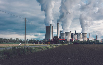 Smoke emitting from factory against cloudy sky