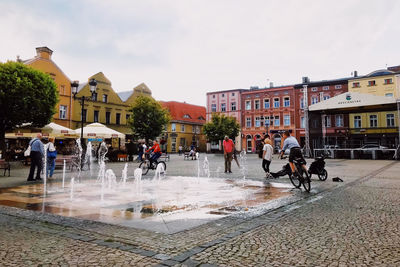 People on wet street against buildings in city