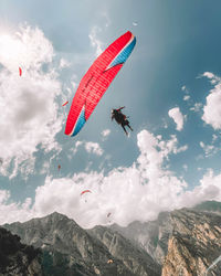 Low angle view of people paragliding against sky