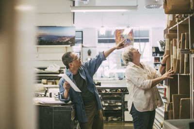 Craftsman pointing while discussing over frames with female coworker at workshop