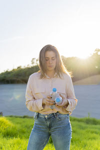 Portrait of young woman at backlight holding two empty plastic bottles