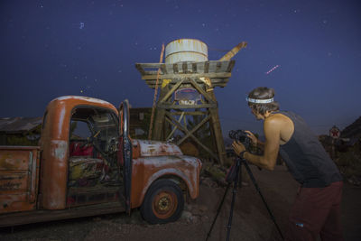 Young photographer capturing vintage car and water tank at night