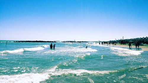 People on beach against clear blue sky