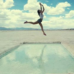 Full length of woman jumping on beach against sky