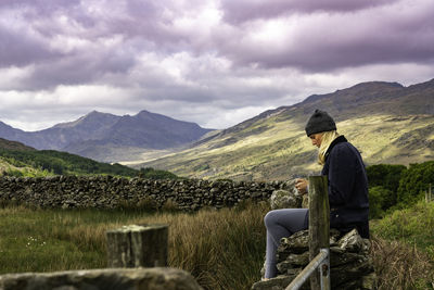 Side view of man looking at mountains against cloudy sky