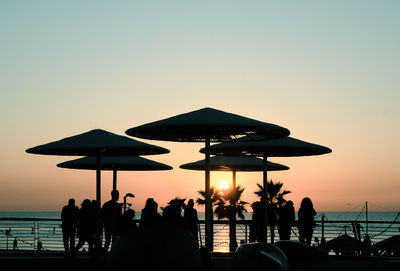 Silhouette people on beach against clear sky during sunset