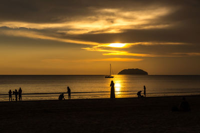 Silhouette people on beach against sky during sunset