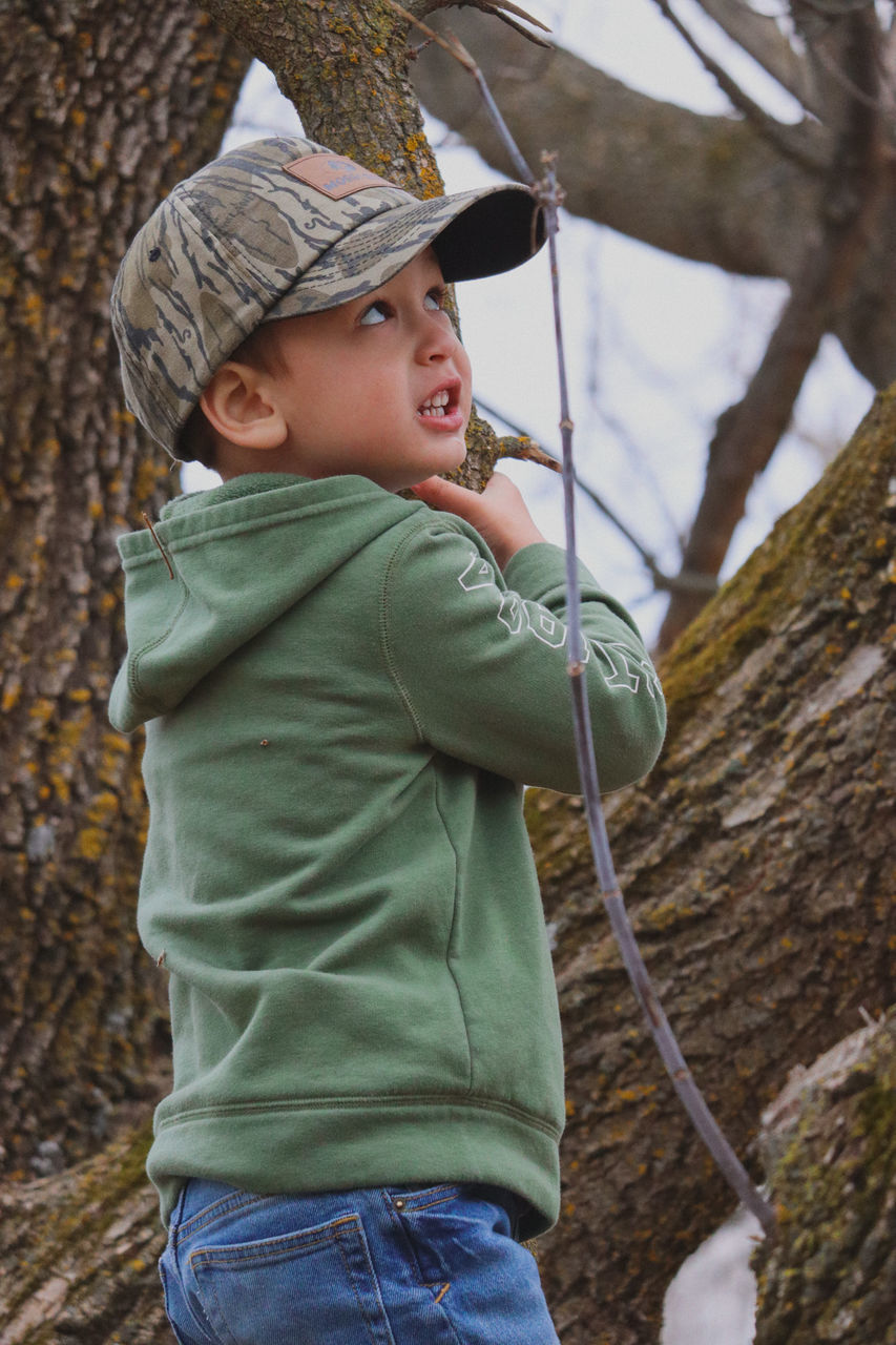 childhood, child, spring, men, one person, tree, clothing, hat, nature, leisure activity, standing, looking, forest, looking up, day, casual clothing, land, outdoors, emotion, side view, tree trunk, three quarter length, plant, toddler, trunk, innocence, holding, adventure, person, portrait, looking away, headwear, climbing, fun, enjoyment