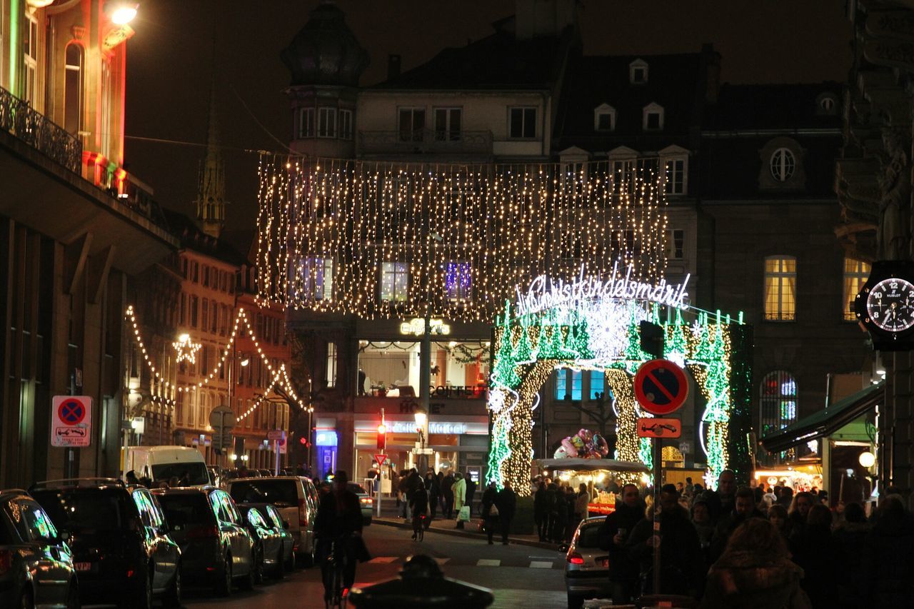 illuminated, night, building exterior, built structure, architecture, city, street, store, lighting equipment, large group of people, city life, men, lifestyles, person, market, celebration, retail, leisure activity, incidental people