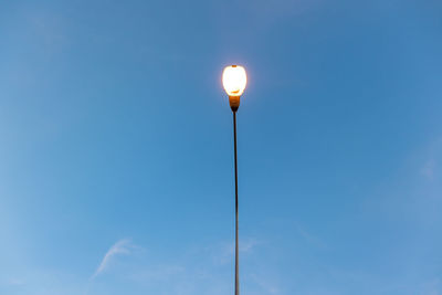 Low angle view of illuminated lamp against blue sky