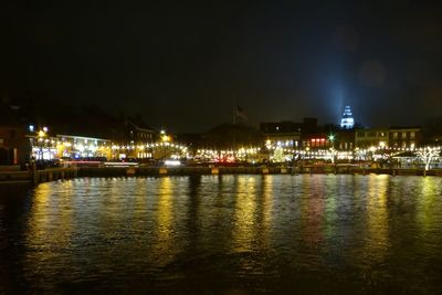 Illuminated buildings by river against sky at night