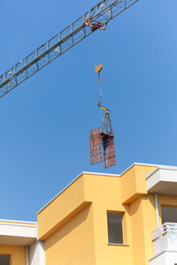 Detail of a crane lifting some pieces of scaffolding over a new building.