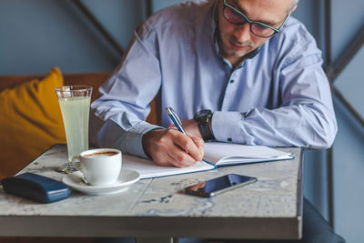 Businessman writing in diary at cafe