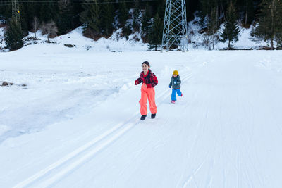 Two children running in the snow valley against forest and mountain background