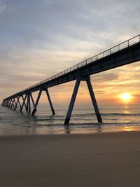 Bridge over calm sea against sky during sunset