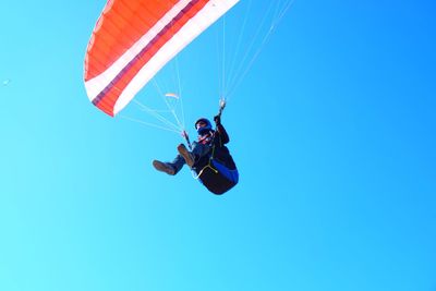 Low angle view of man paragliding against clear blue sky