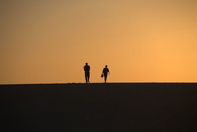 Silhouette of people walking against sky during sunset