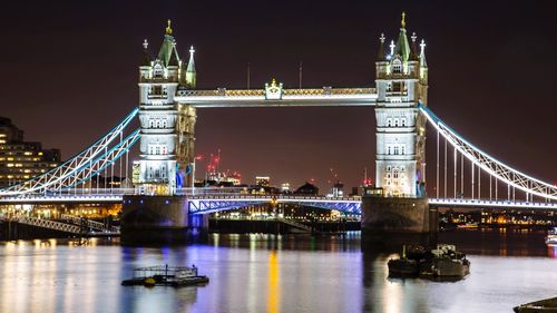 Illuminated bridge over river in city at night