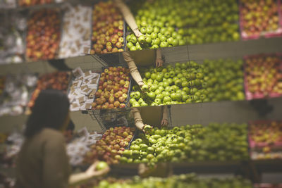 Low angle view of woman choosing apples, fruits reflecting in supermarket mirrors