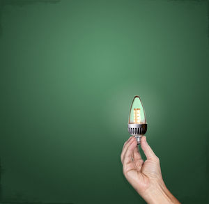 Person holding light bulb against green background