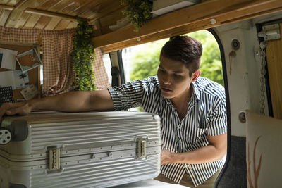 Young man keeping suitcase in motor van