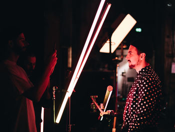 Young man standing by illuminated lights at night