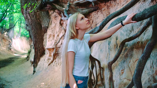 Full length of young woman standing by tree trunk