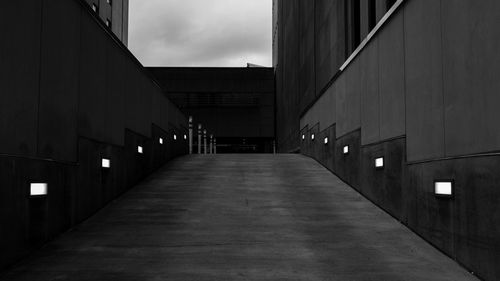 Illuminated footpath amidst buildings against sky in city