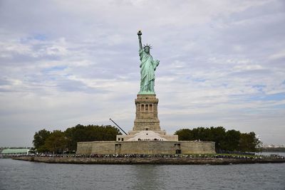 Statue of liberty by hudson river against cloudy sky