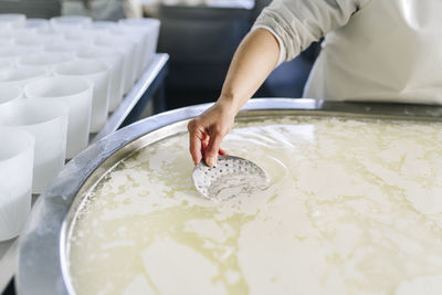 Female chef using straining spoon while making cheese in dairy factory