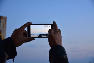 Low section of person photographing mobile phone against sky