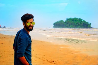 Portrait of young man wearing sunglasses while standing at beach