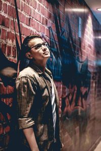 Young man looking away while standing against graffiti wall