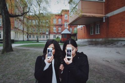 Female friends taking selfie with smart phone while standing against buildings