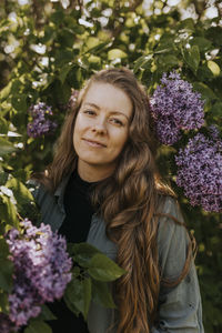 Portrait of smiling woman standing against lilac bush