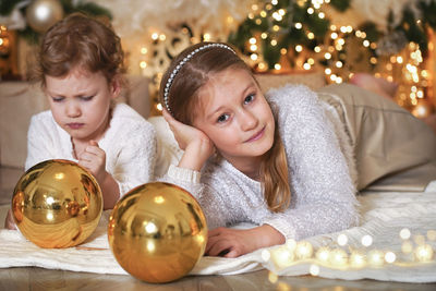 Portrait of girl lying on floor with sister against christmas decoration