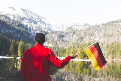 Rear view of man with flags standing against snowcapped mountains