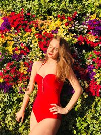 Beautiful woman wearing red swimsuit standing against flowering plants