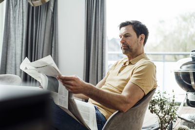 Mature man reading newspaper in living room at home