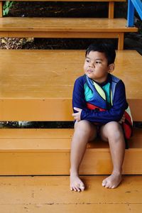 Full length of cute boy sulking while looking away on wooden steps