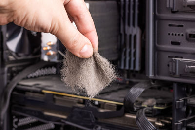 Bare caucasian hand holding dust clog in front of opened pc case during maintenance