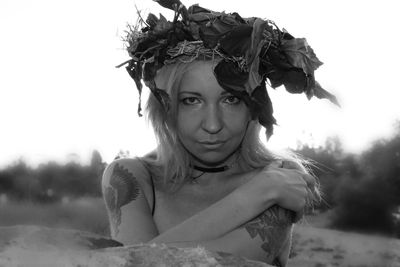 Portrait of shirtless woman with tattoo wearing leaves wreath against sky