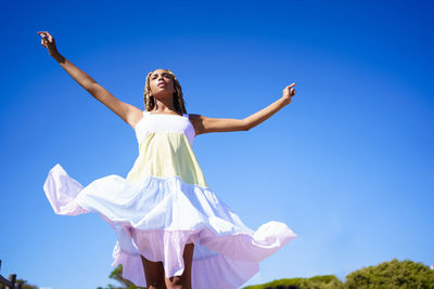 Full length of woman with arms raised standing against blue sky